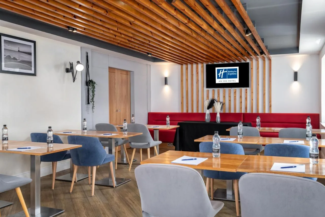 a restaurant with wooden tables and chairs and a red couch at Holiday Inn Express Aberdeen City Centre by IHG in Aberdeen